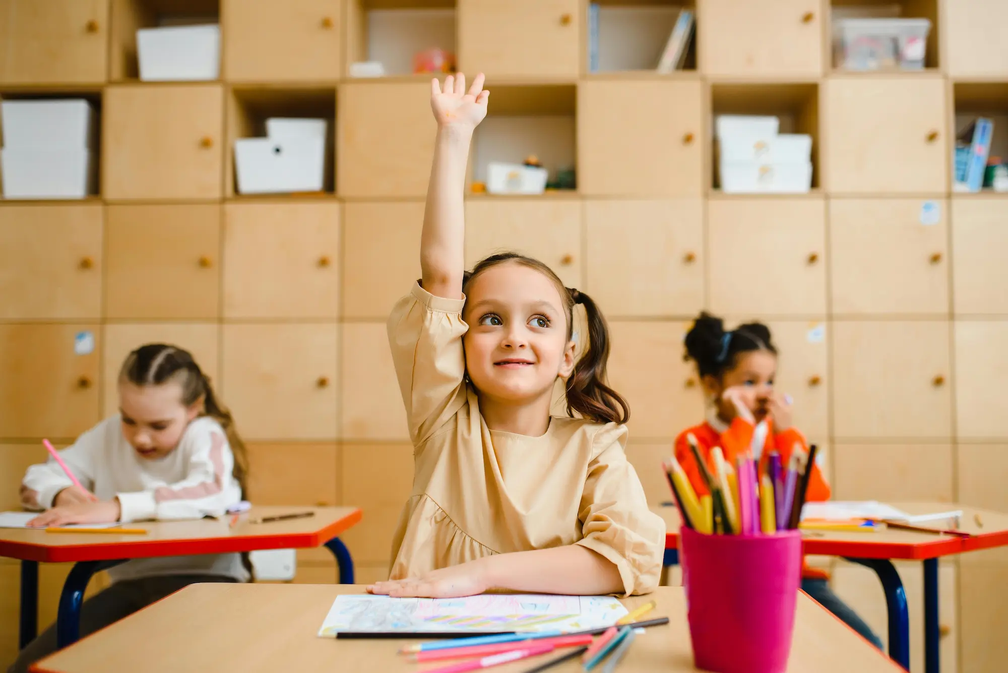 Enfant à l’école levant la main, symbole de confiance en soi et soutien aux enfants perfectionnistes.